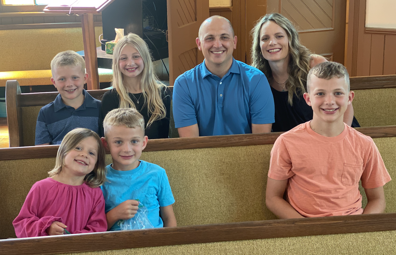 Tommy with his wife and five kids sitting together in a church pew