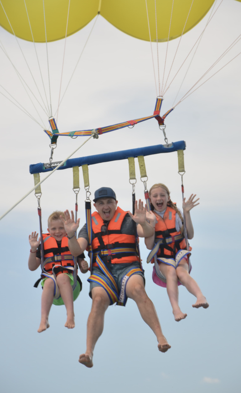 Tommy parasailing high above the water with two of his kids
